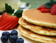 A stack of pancakes with blueberries and strawberries accenting the plate.