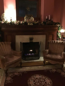 Dark pink tones on the walls set off the marble on this mahagony fireplace with lit fire and low victorian chairs. 